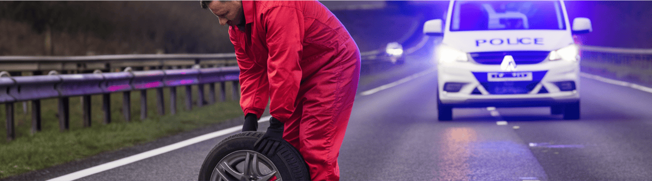 A man changing a tyre on a motorway with police car in background. 