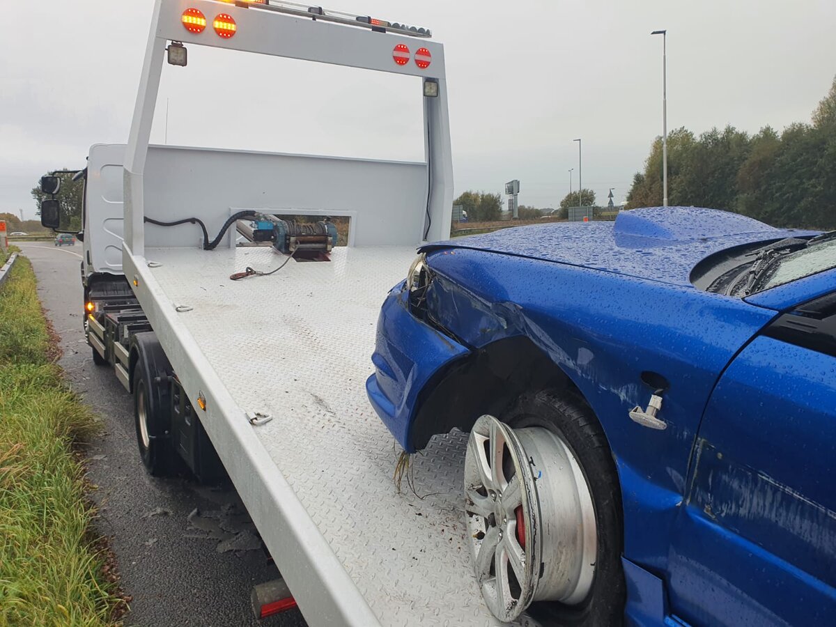 Accident-damaged blue Subaru Impreza loaded onto a white recovery truck after a side impact.