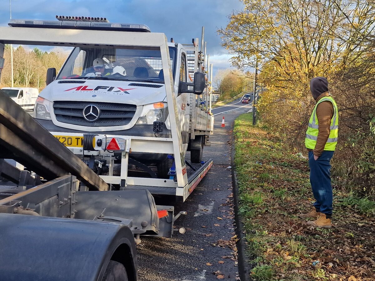 Alfix-branded Mercedes recovery truck loading a vehicle on a roadside in autumn with a Breakdown Man operator in high-vis stood beside it.