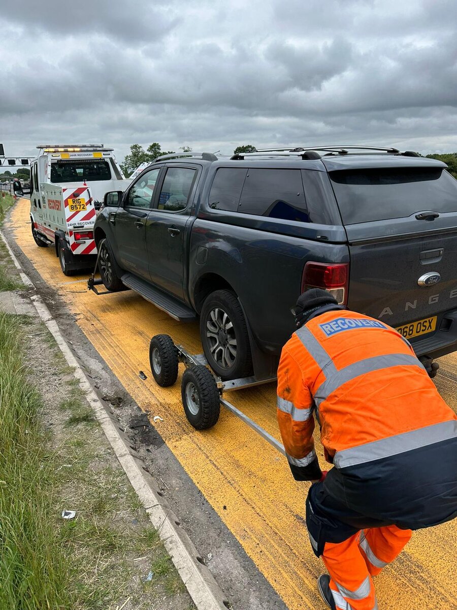Breakdown Man recovering a black Ford Ranger 4x4 on tow dollies on the M62 motorway hard shoulder.