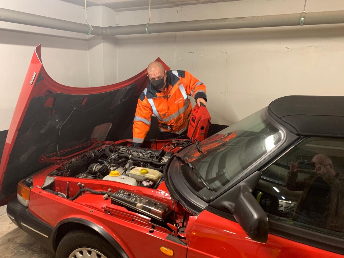 A Breakdown Man technician in hi-vis using a red Snap-on jump pack on a red Saab convertible with the bonnet open.
