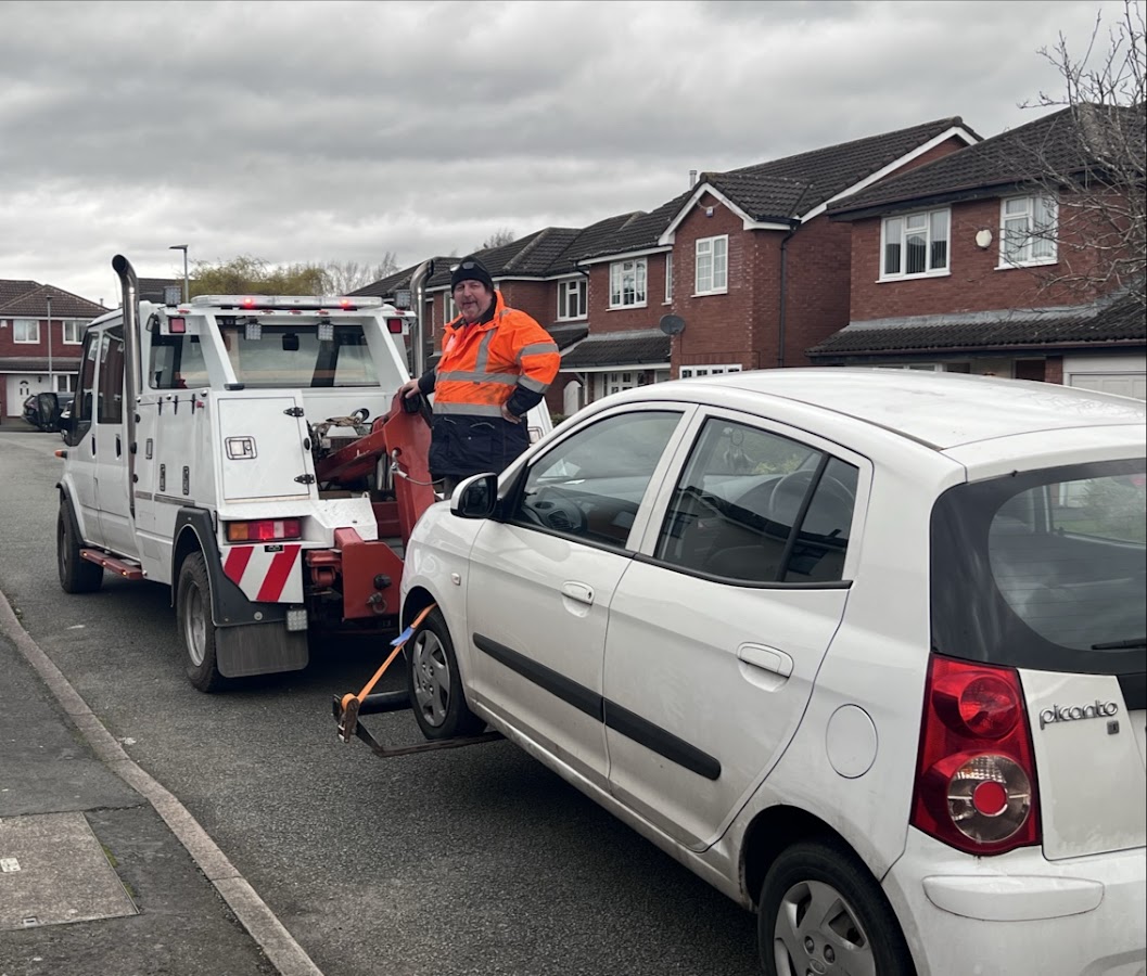 A Breakdown Man technician towing a Kia Picanto on a residential street.
