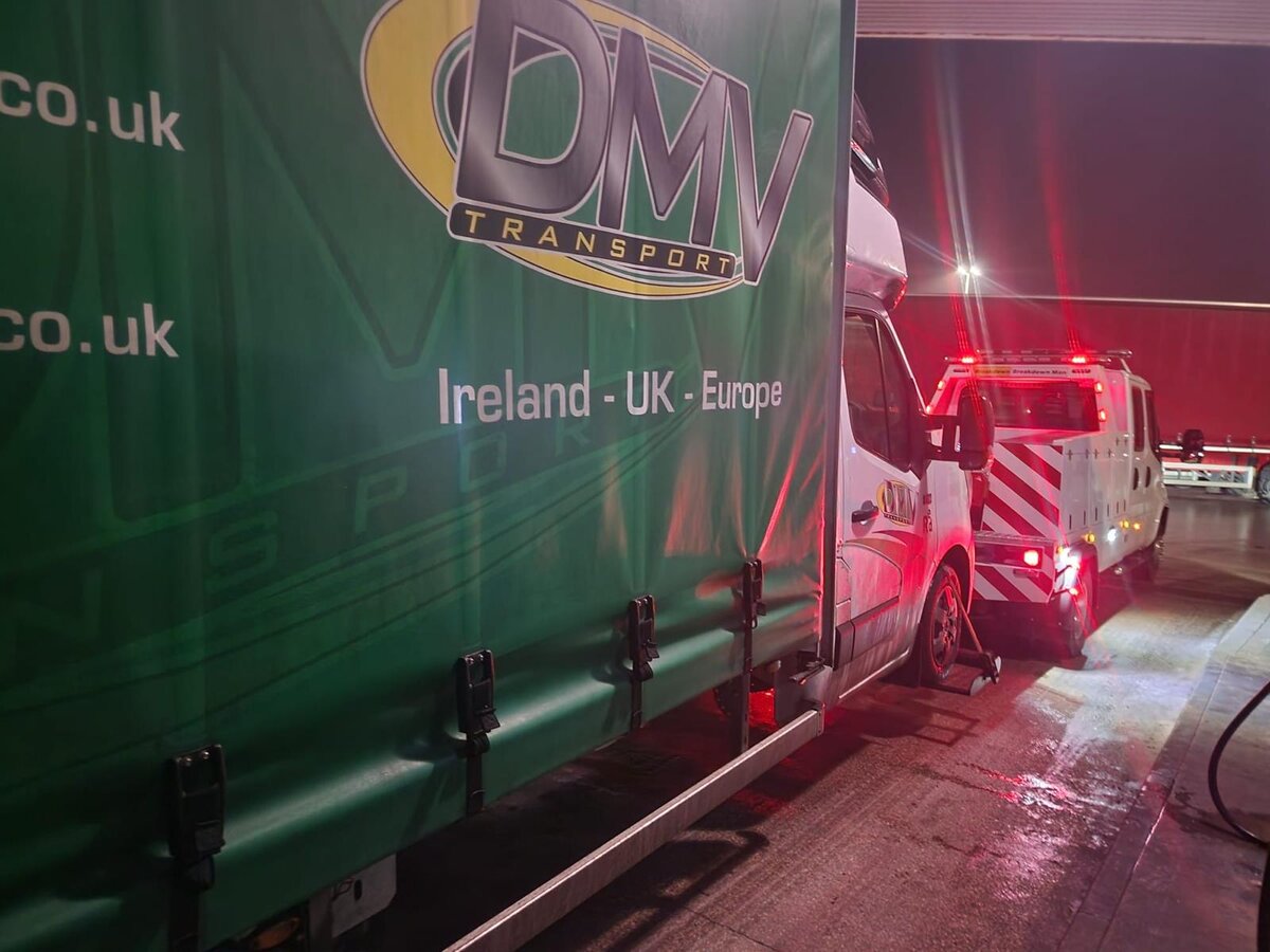 White Renault Master van being recovered onto Breakdown Man's recovery truck beside a DMV Transport curtainsider trailer at night.