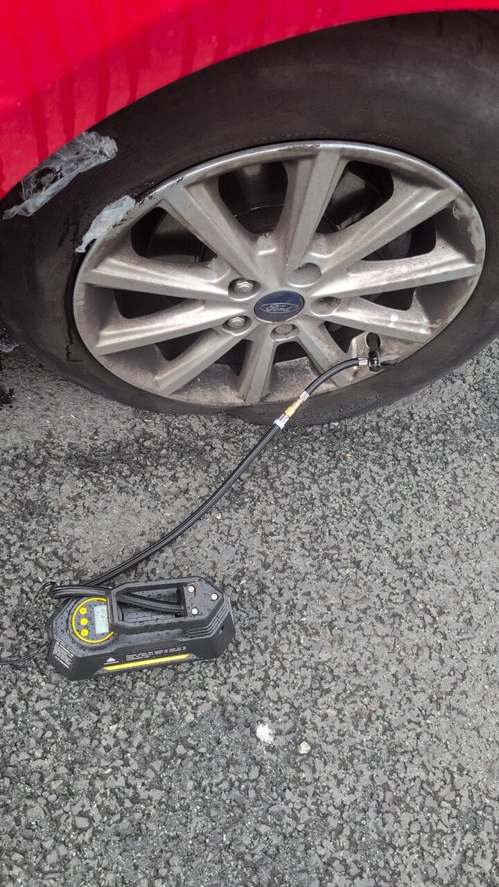Flat alloy wheel on a red car being inflated with a foot pump on a roadside callout