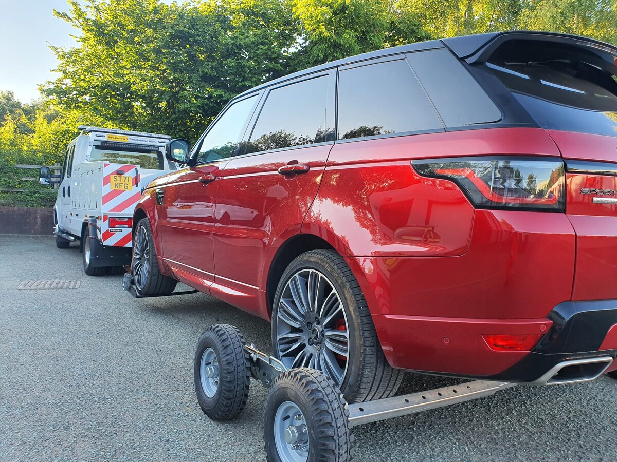 Red Range Rover Sport secured on a wheel-lift recovery dolly behind the Breakdown Man recovery truck on a summer day at the depot.