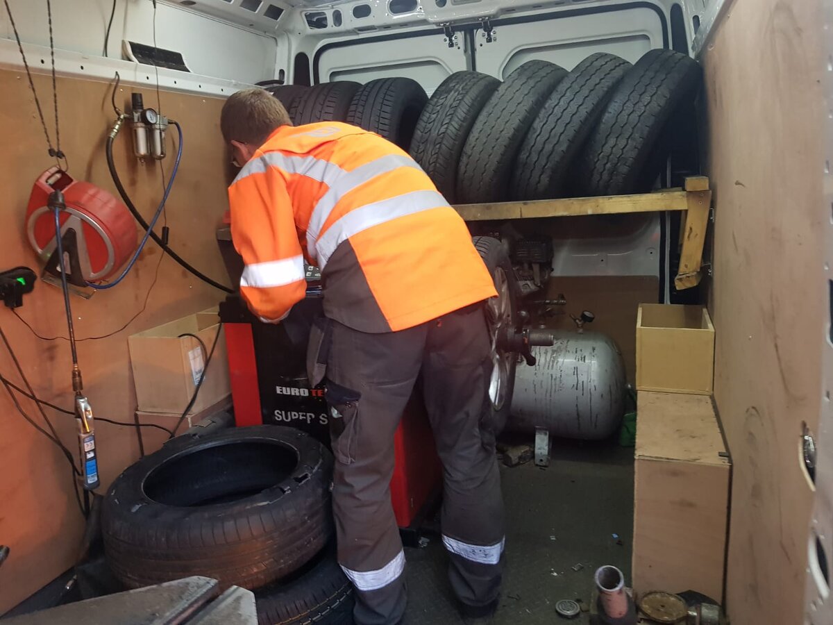 Mobile tyre fitter in orange hi-vis working at a tyre changing machine inside a fully kitted Breakdown Man tyre van.