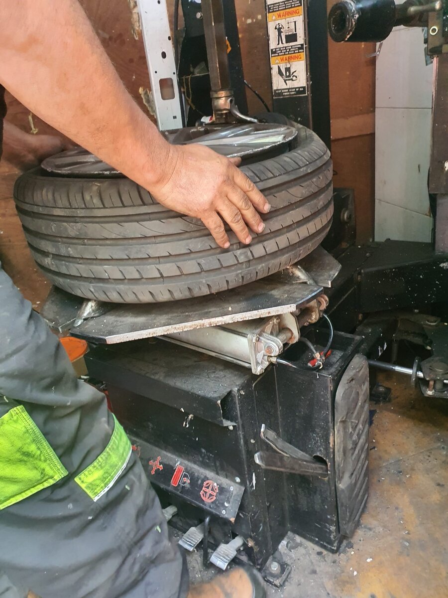 Hands fitting a tyre onto a wheel rim on a tyre-changing machine at the Breakdown Man workshop.