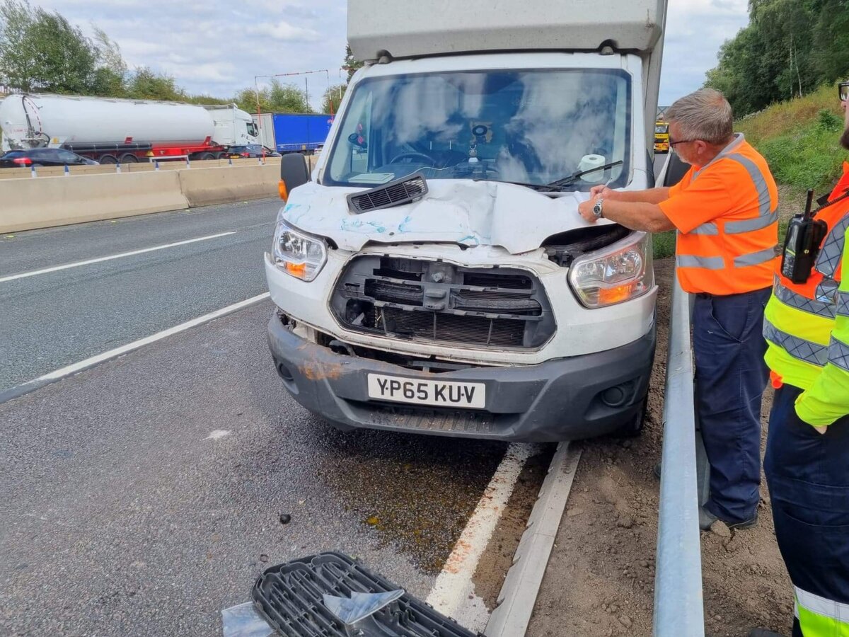 Front-end damaged white Ford Transit van YP65 KUV on the motorway hard shoulder with a traffic officer assisting.