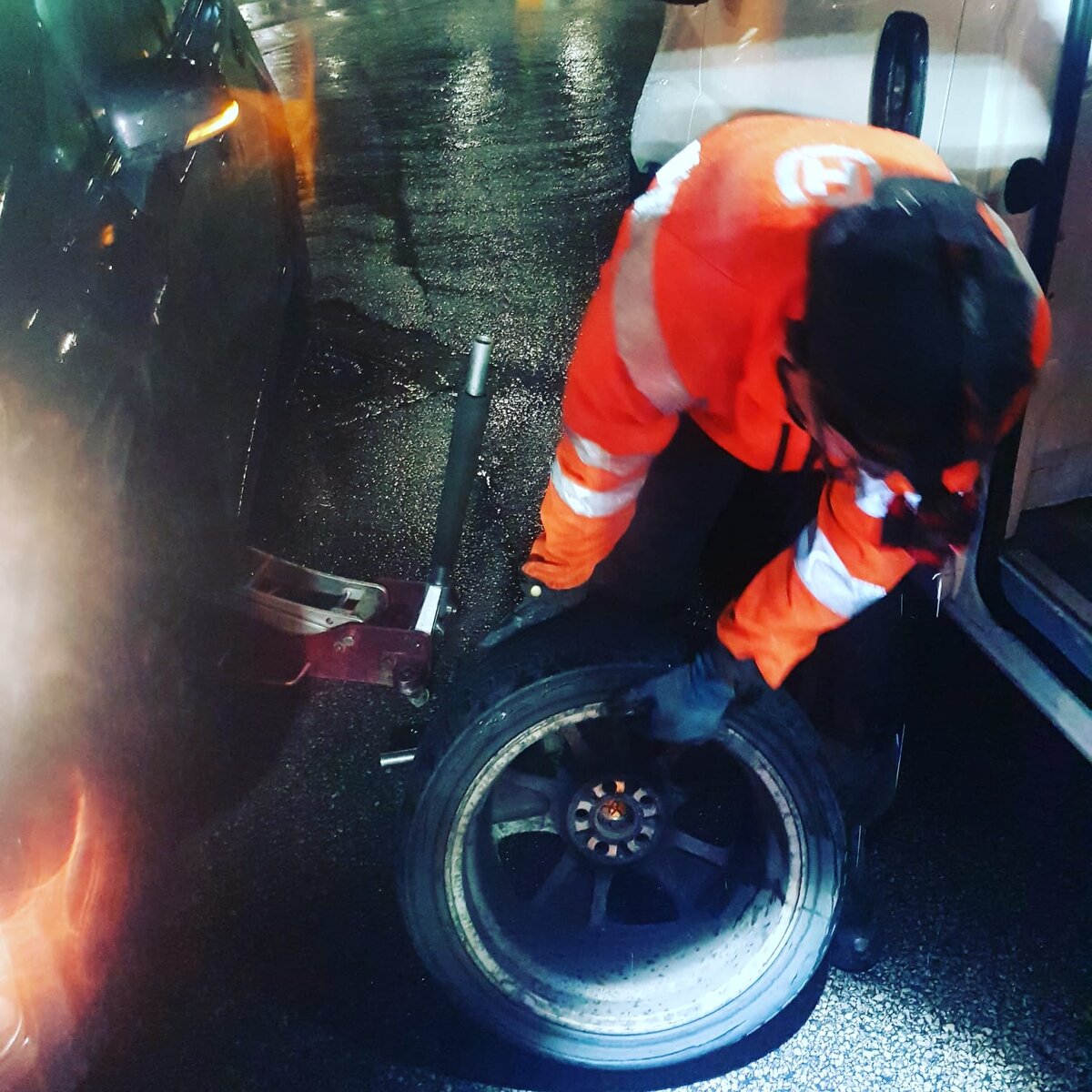 Simon changing a wheel at night on a wet road in Breakdown Man hi-vis jacket.