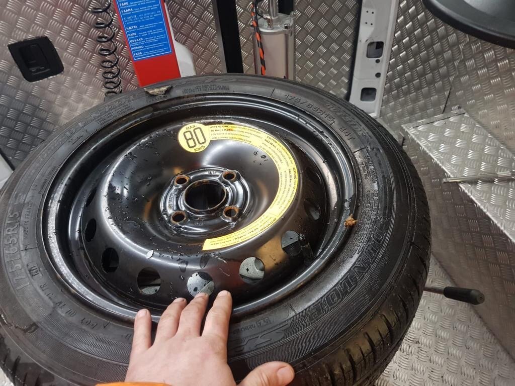 Punctured space-saver spare wheel laid on the chequered floor of a Breakdown Man recovery truck during a roadside callout.