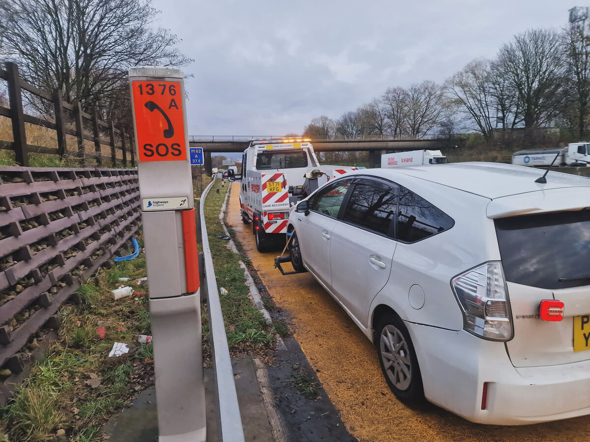 Breakdown Man recovering a white Toyota beside a motorway SOS phone — 24-hour cover serving Tyldesley.