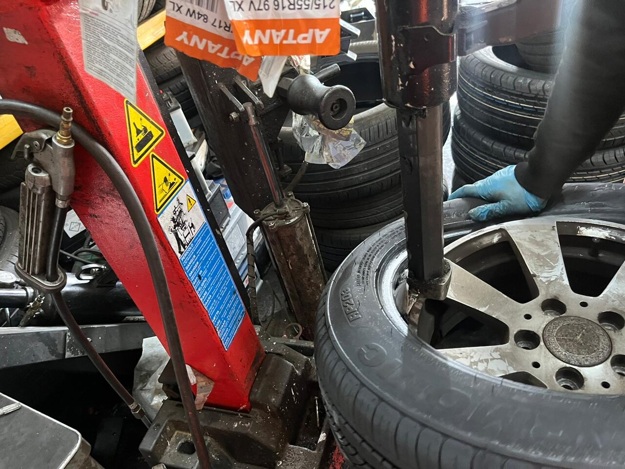 Wheel mounted on a tyre changing machine with a fitter's gloved hand guiding a fresh tyre into place