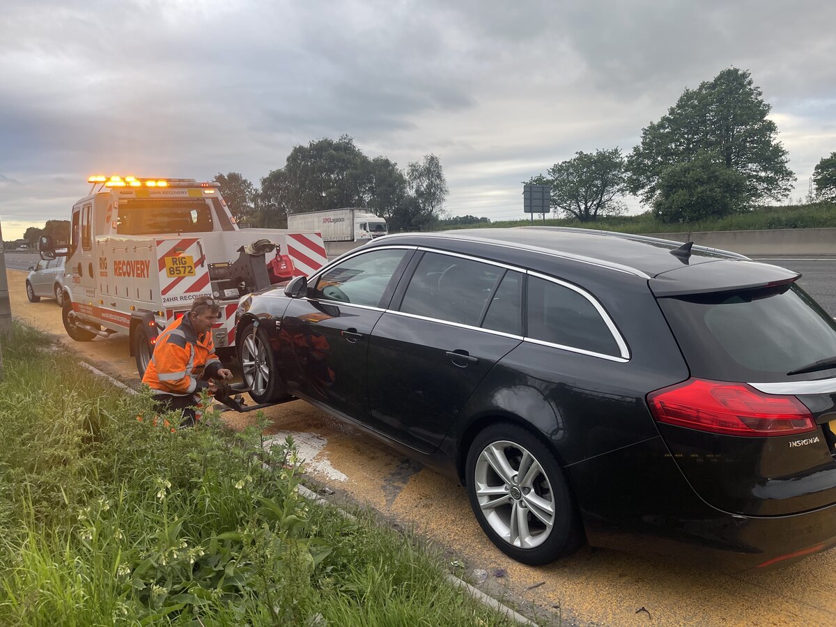Black Vauxhall Insignia estate on the motorway grass verge, Breakdown Man fitting front-end skates ready to tow.