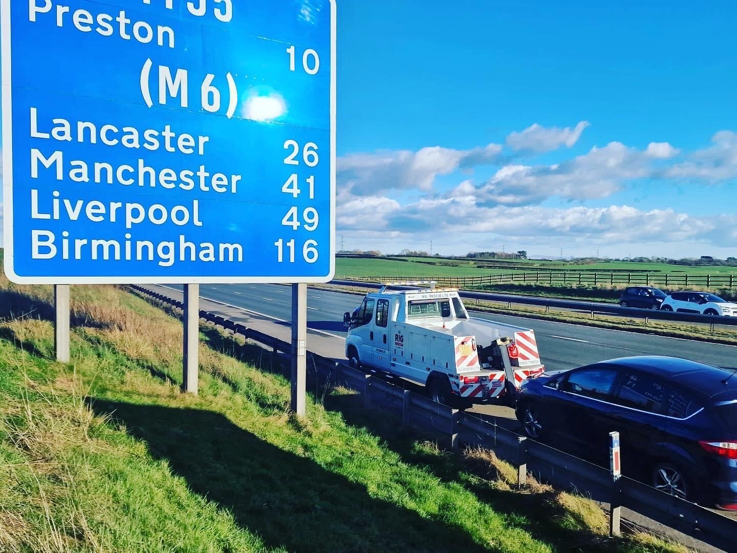 Breakdown Man recovery truck on the motorway alongside a blue motorway directional sign.