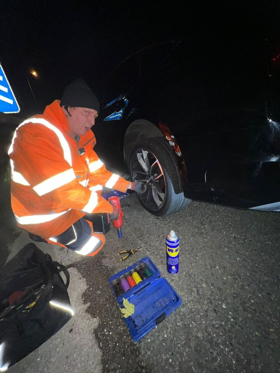 Simon working on a car's alloy wheel at the roadside at night under hi-vis lighting.