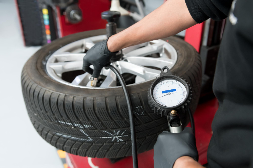 A hand-held pressure gauge on a summer tyre fitted to an alloy wheel.